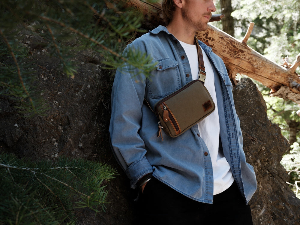 Sea Dragon Dreams pewter green waxed canvas sling bag with brown leather accents worn crossbody by a man outdoors.