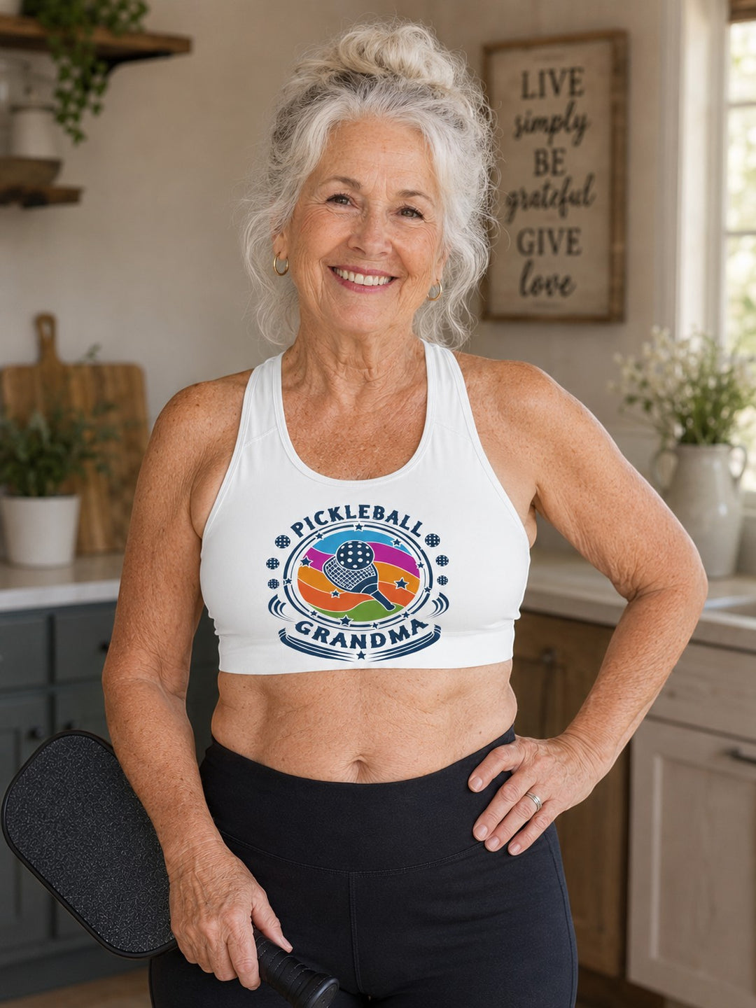 Sea Dragon Dreams white sports bra with Pickleball Grandma graphic worn by a smiling woman holding a pickleball paddle.