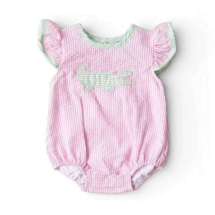 Sea Dragon Dreams baby girl bubble romper in pink seersucker with a green alligator appliqué and flutter sleeves.