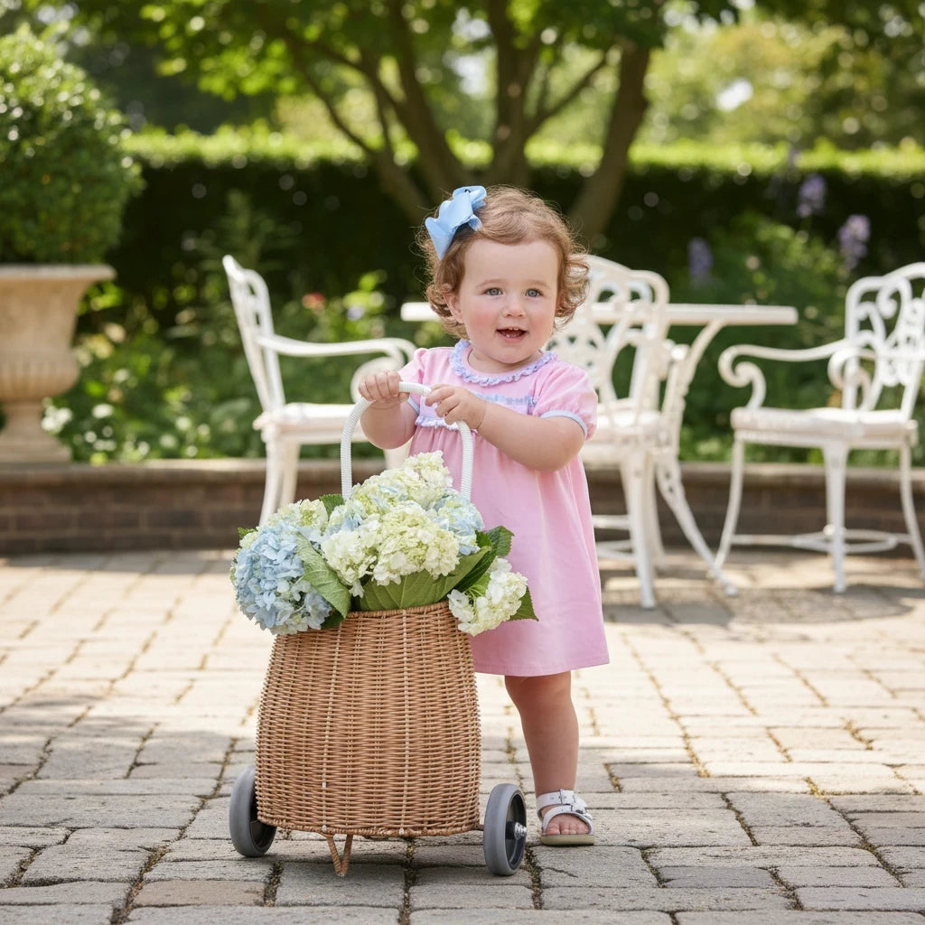 Toddler girl wearing a Sea Dragon Dreams pink puff-sleeve dress with ruffle trim and bow detail, standing in a garden.