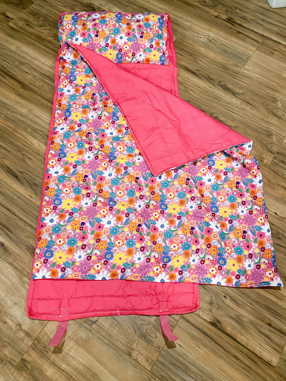 Sea Dragon Dreams pink floral kids nap mat with an attached blanket and built-in pillow on a wooden floor.