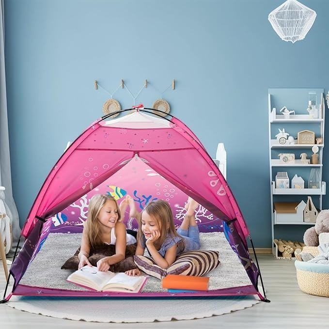 Sea Dragon Dreams pink mermaid pop-up play tent with two girls reading inside on a cozy rug in a bedroom.