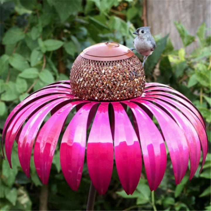 Sea Dragon Dreams petal-shaped metal bird feeder in vibrant pink with a central mesh seed container in a garden setting