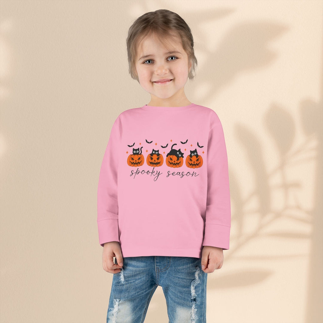 Toddler wearing a Sea Dragon Dreams pink long sleeve Halloween tee with a pumpkin and black cat print and blue jeans.