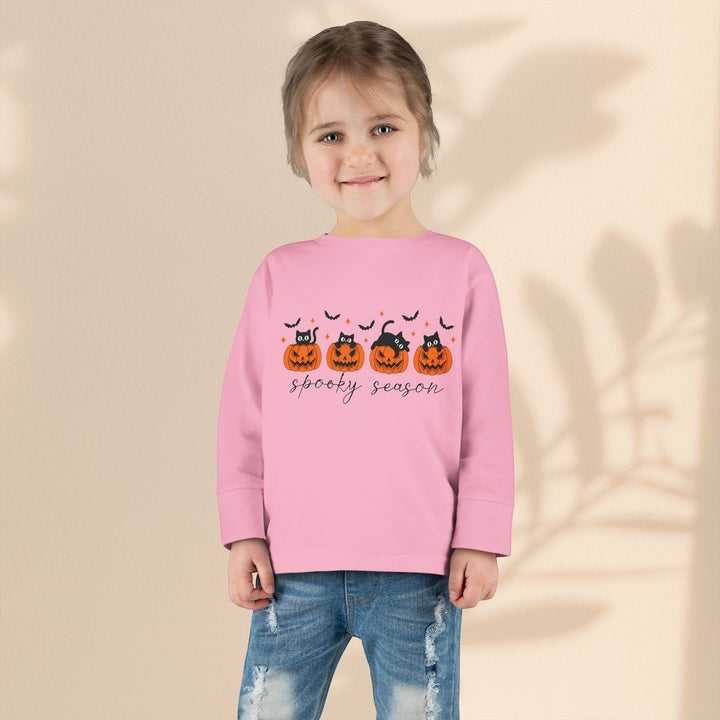 Toddler wearing a Sea Dragon Dreams pink long sleeve Halloween tee with a pumpkin and black cat print and blue jeans.