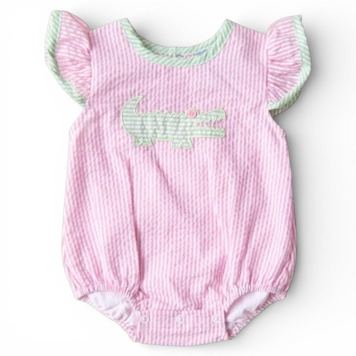 Sea Dragon Dreams baby girl bubble romper in pink seersucker with a green alligator appliqué and flutter sleeves.