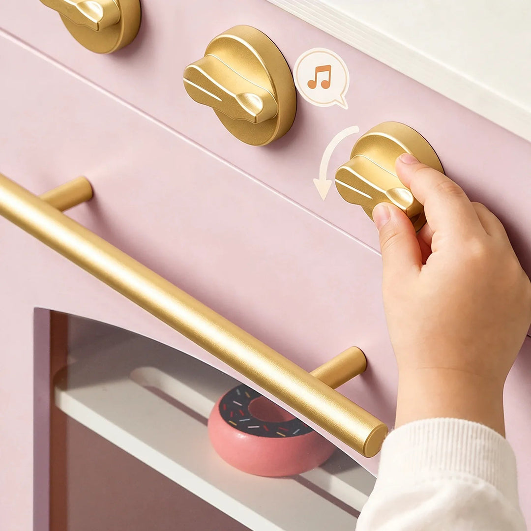 Sea Dragon Dreams Tiny Land wooden play kitchen in sakura pink with gold knobs and handle being turned by a child