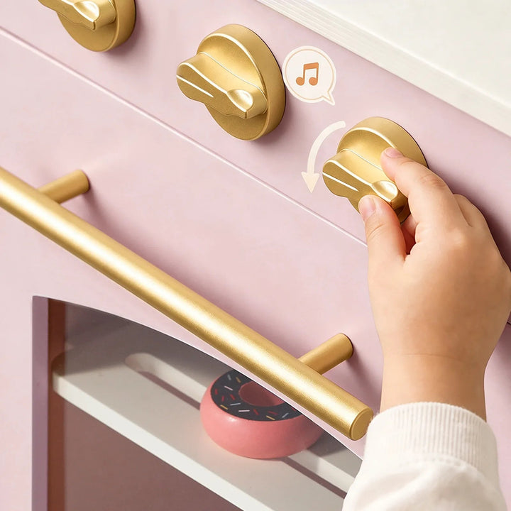 Sea Dragon Dreams Tiny Land wooden play kitchen in sakura pink with gold knobs and handle being turned by a child