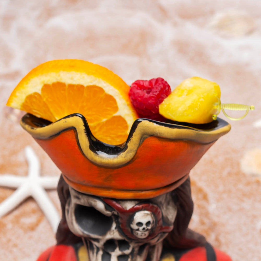 Sea Dragon Dreams BarConic pirate skeleton tiki mug filled with a tropical cocktail, garnished with fruit on a beach.