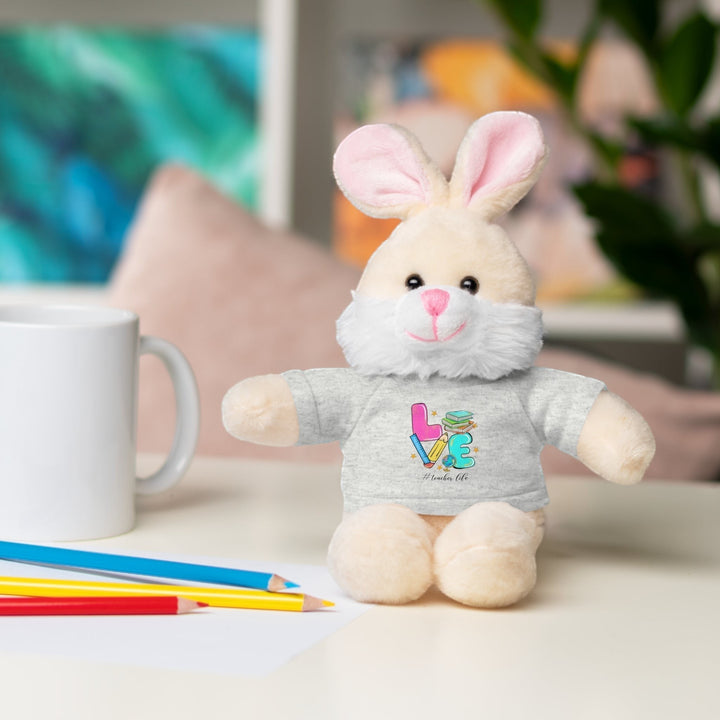 Sea Dragon Dreams plush bunny stuffed animal wearing a grey cotton tee with Love Teacher Life graphic on a desk.