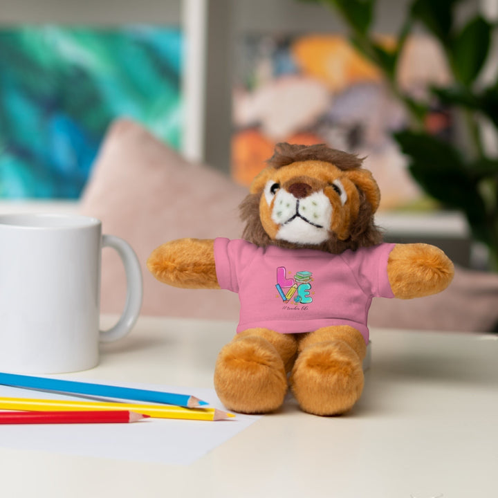 Sea Dragon Dreams plush lion stuffed animal wearing a pink t-shirt with Love Teacher Life graphic on a desk