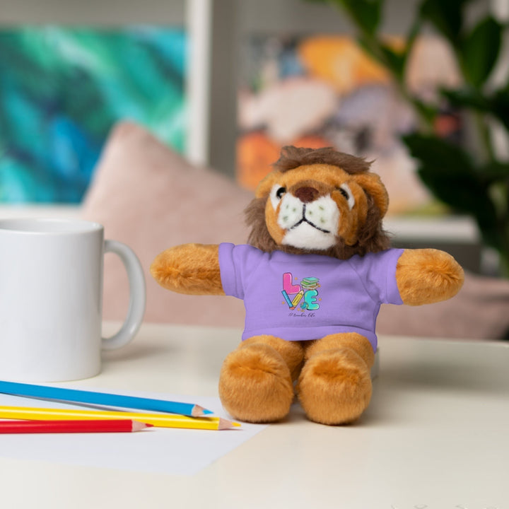 Sea Dragon Dreams plush lion stuffed animal wearing a purple t-shirt with Love Teacher Life text on a desk