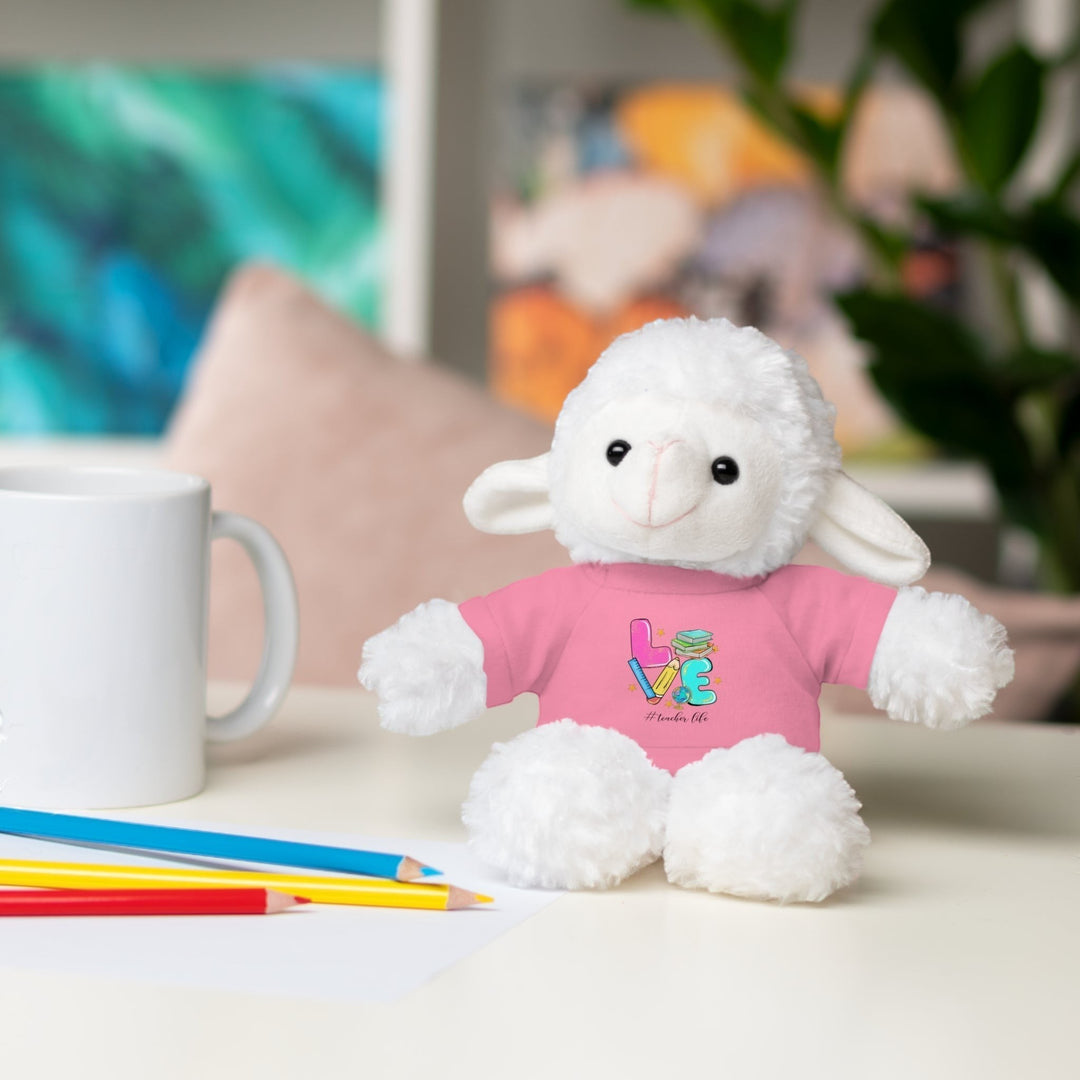 Sea Dragon Dreams plush sheep stuffed animal wearing a pink t-shirt with Love Teacher Life graphic on a desk