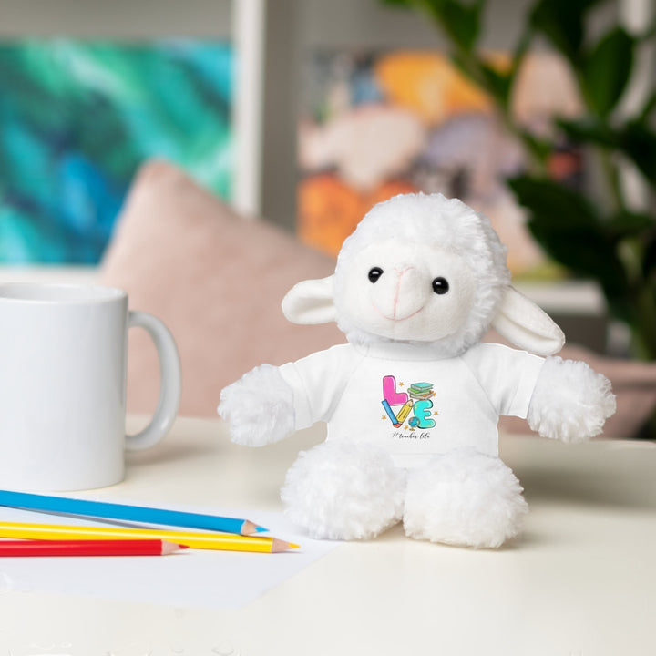 Sea Dragon Dreams plush sheep toy wearing a white t-shirt with Love Teacher Life graphic on a desk with pencils