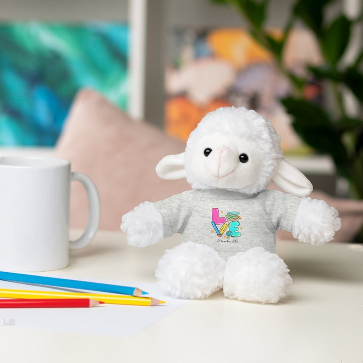 Sea Dragon Dreams plush sheep toy wearing a grey t-shirt with Love Teacher Life text, sitting on a desk with pencils.
