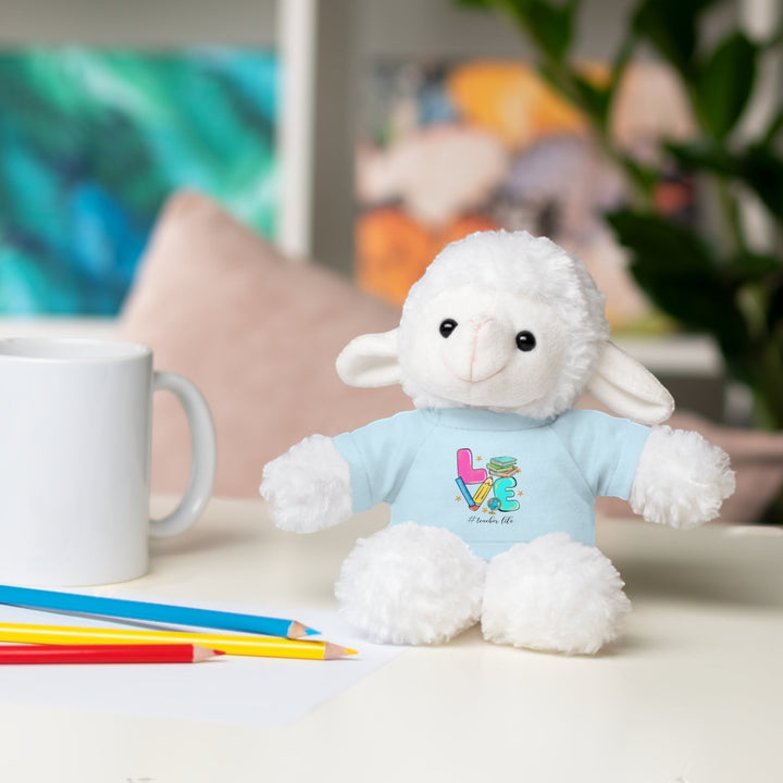 Sea Dragon Dreams plush sheep toy wearing a light blue t-shirt with Love Teacher Life graphic on a desk with pencils