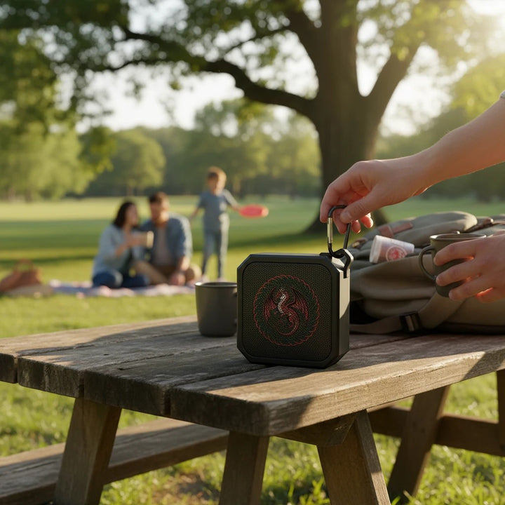 Sea Dragon Dreams portable Bluetooth speaker with dragon emblem on a wooden picnic table in a park setting.