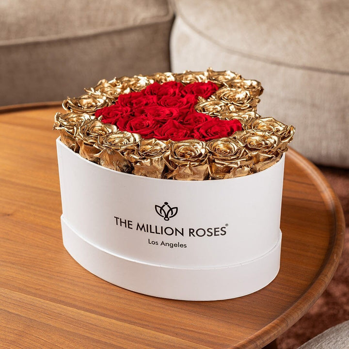 Sea Dragon Dreams heart-shaped white box filled with preserved red roses and 24K gold-dipped roses on a wooden table.