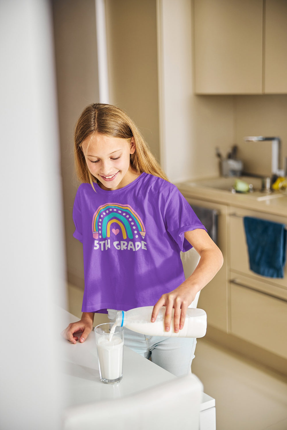 Sea Dragon Dreams purple youth t-shirt with a rainbow 5th grade graphic worn by a girl pouring milk in a kitchen