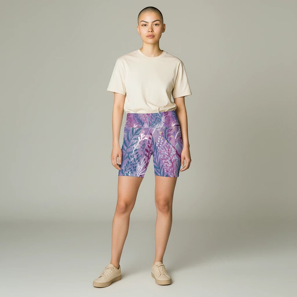 Model wearing Sea Dragon Dreams purple seaweed print polyester workout shorts with a beige t-shirt and sneakers.