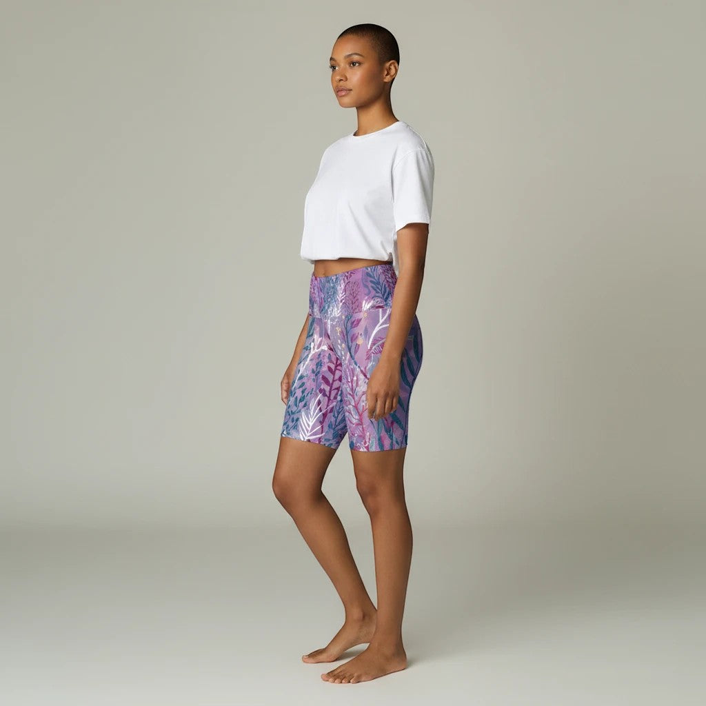 Model wearing Sea Dragon Dreams purple seaweed print polyester workout shorts with a white crop top, side view.