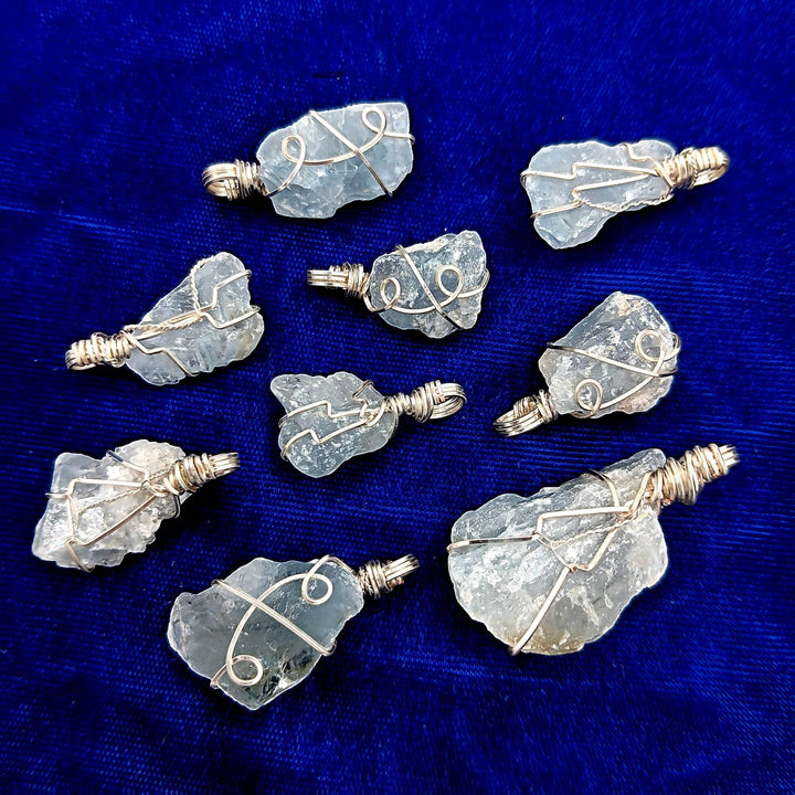 Sea Dragon Dreams raw celestite crystal pendants with silver-plated wire wrapping on a blue velvet background.