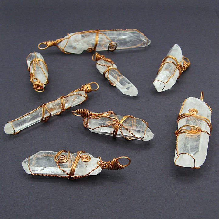 Sea Dragon Dreams raw clear quartz crystal pendants wrapped in rustic copper wire, displayed on a dark background.