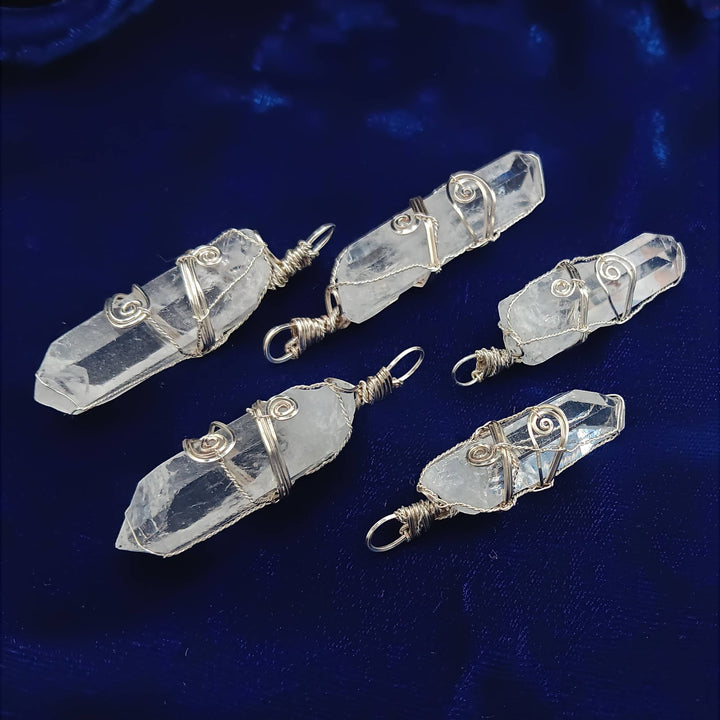 Sea Dragon Dreams raw clear quartz crystal pendants with silver-plated wire wrapping on a deep blue velvet background.