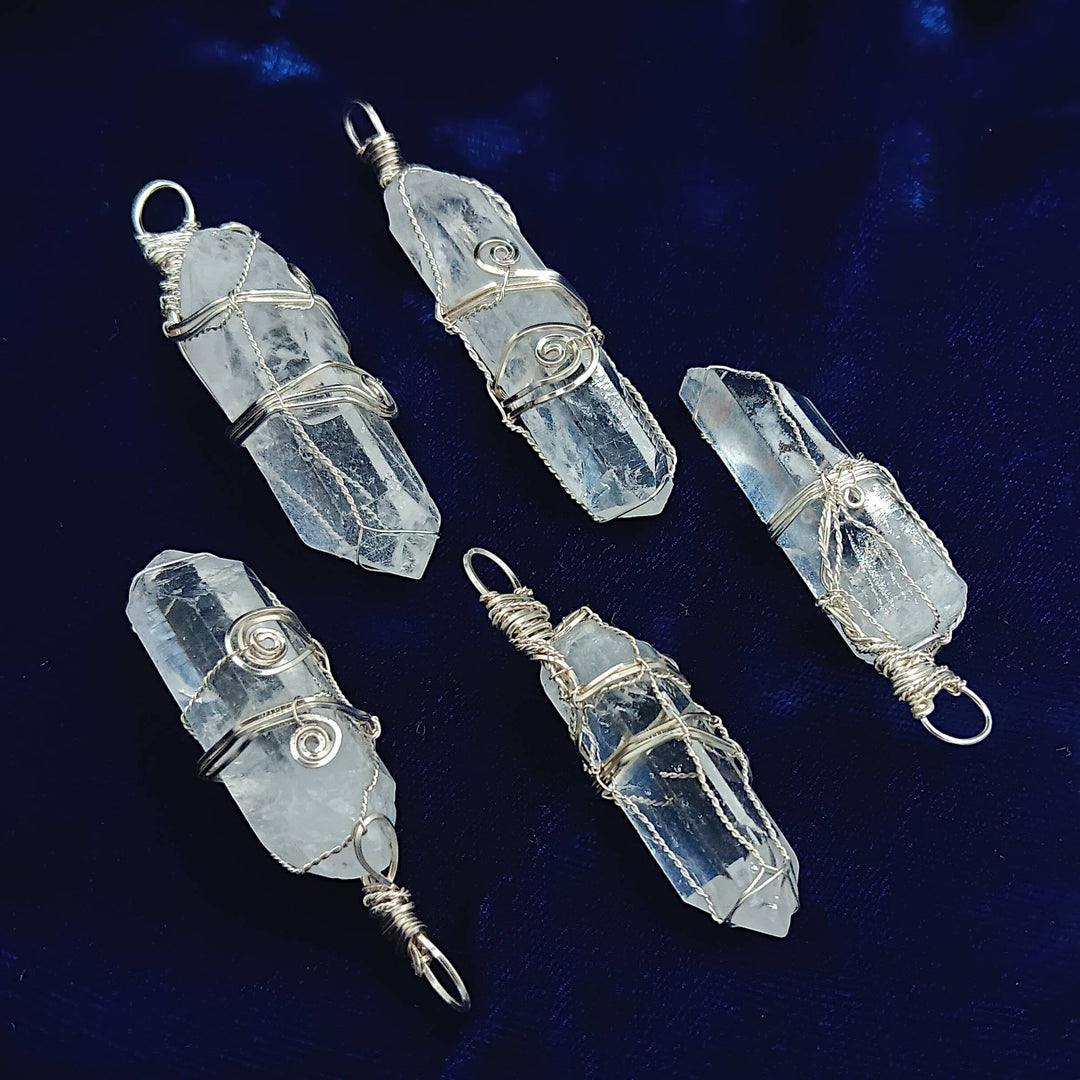 Sea Dragon Dreams raw clear quartz crystal pendants with intricate silver-plated wire wrapping on dark blue velvet.