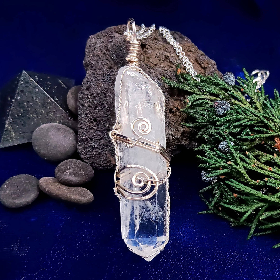 Sea Dragon Dreams raw clear quartz crystal pendant with intricate silver-plated wire wrapping on a dark blue background