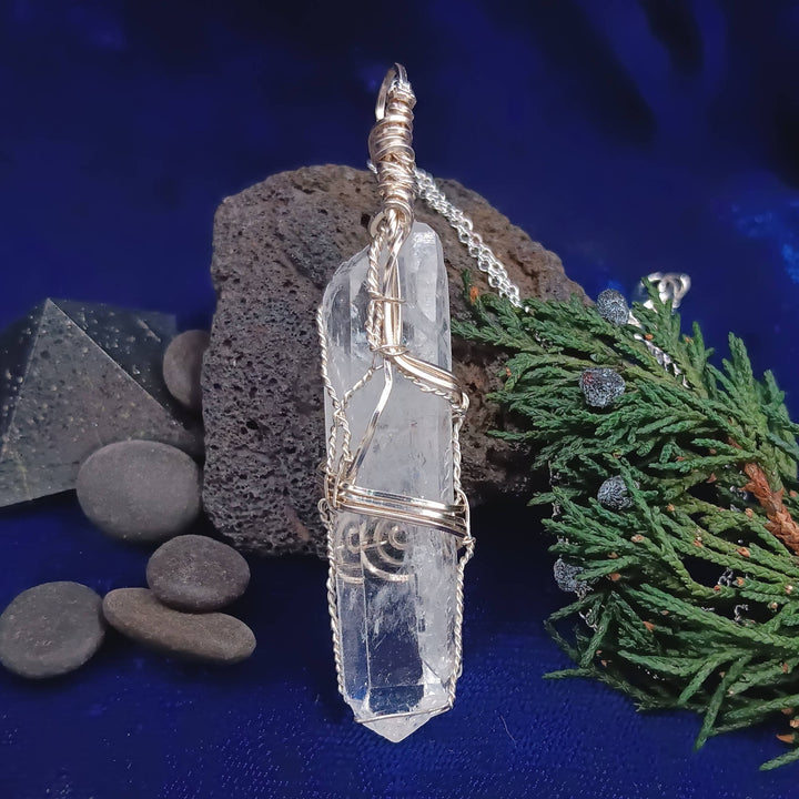 Sea Dragon Dreams raw clear quartz crystal pendant hand-wrapped in silver-plated wire on a dark blue background.