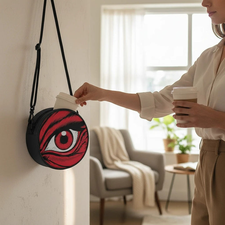 Sea Dragon Dreams round canvas satchel bag with a red eye design, hanging on a wall with a shoulder strap.