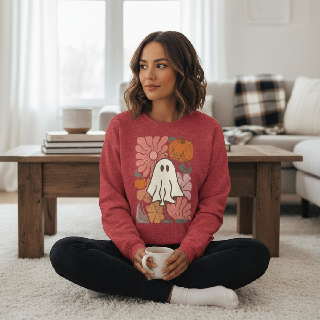 Woman wearing a Sea Dragon Dreams red crewneck sweatshirt with a ghost and floral graphic while sitting on a rug.