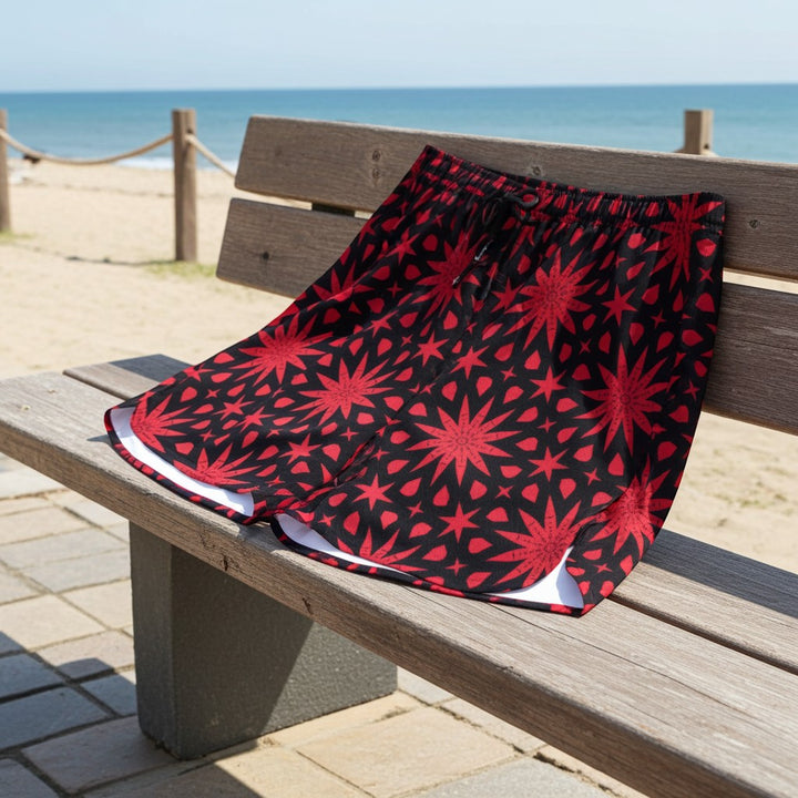 Sea Dragon Dreams men's polyester shorts with a bold red star pattern on a black background, displayed on a beach bench.