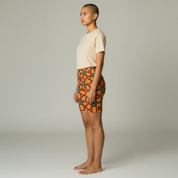 Model wearing Sea Dragon Dreams red and yellow patterned polyester workout shorts with a neutral t-shirt.