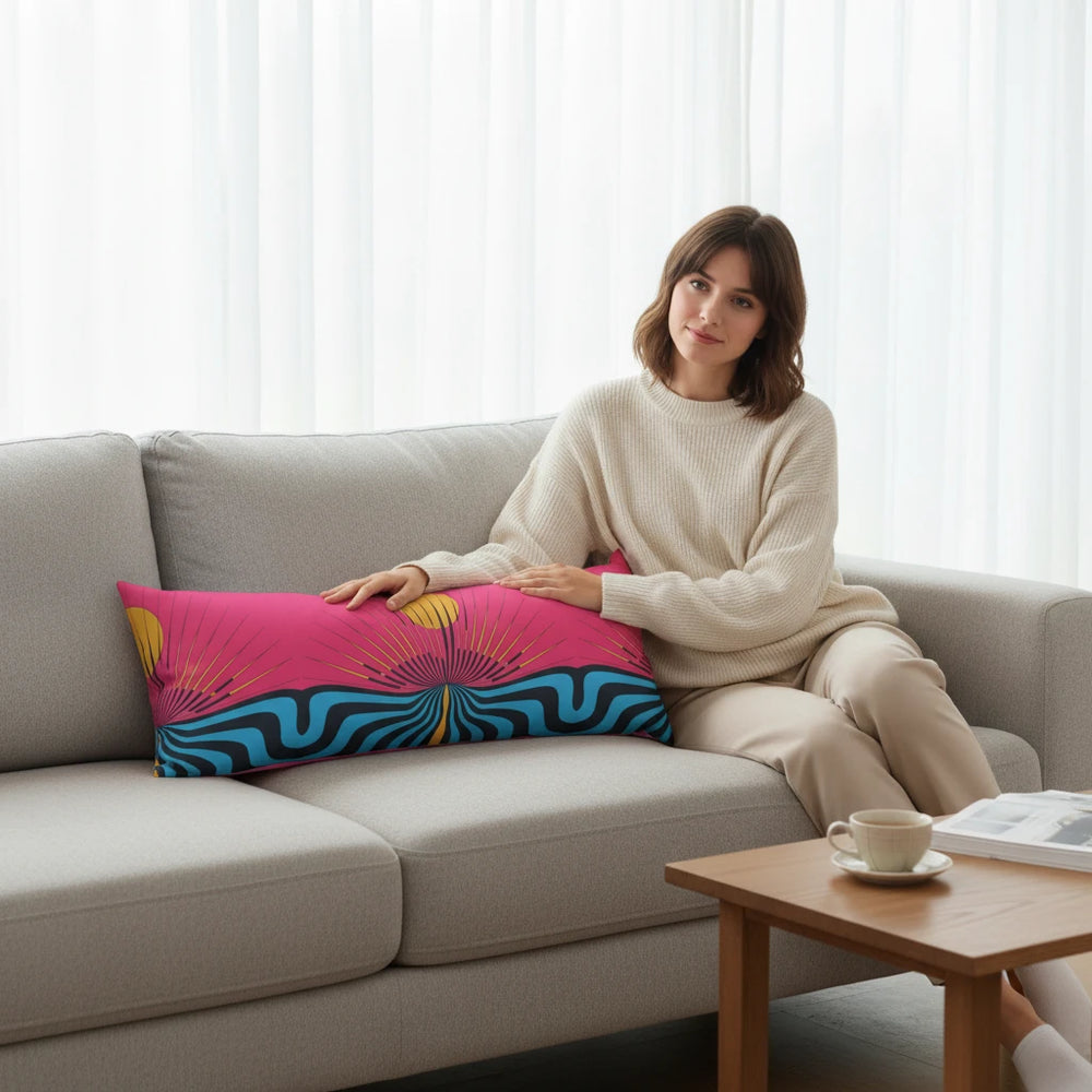 Sea Dragon Dreams body pillow with magenta sun and teal wave print on a grey sofa with a woman sitting beside it.