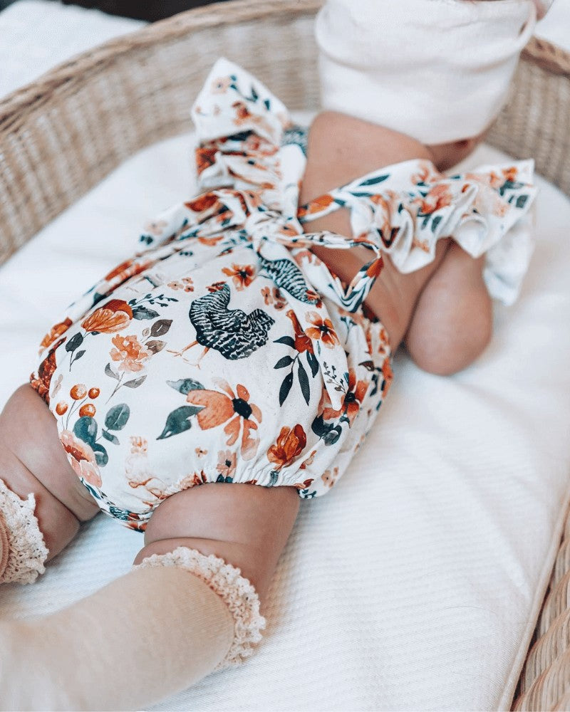 Sea Dragon Dreams baby romper with chicken and floral print, featuring ruffle back straps and a tie bow detail.