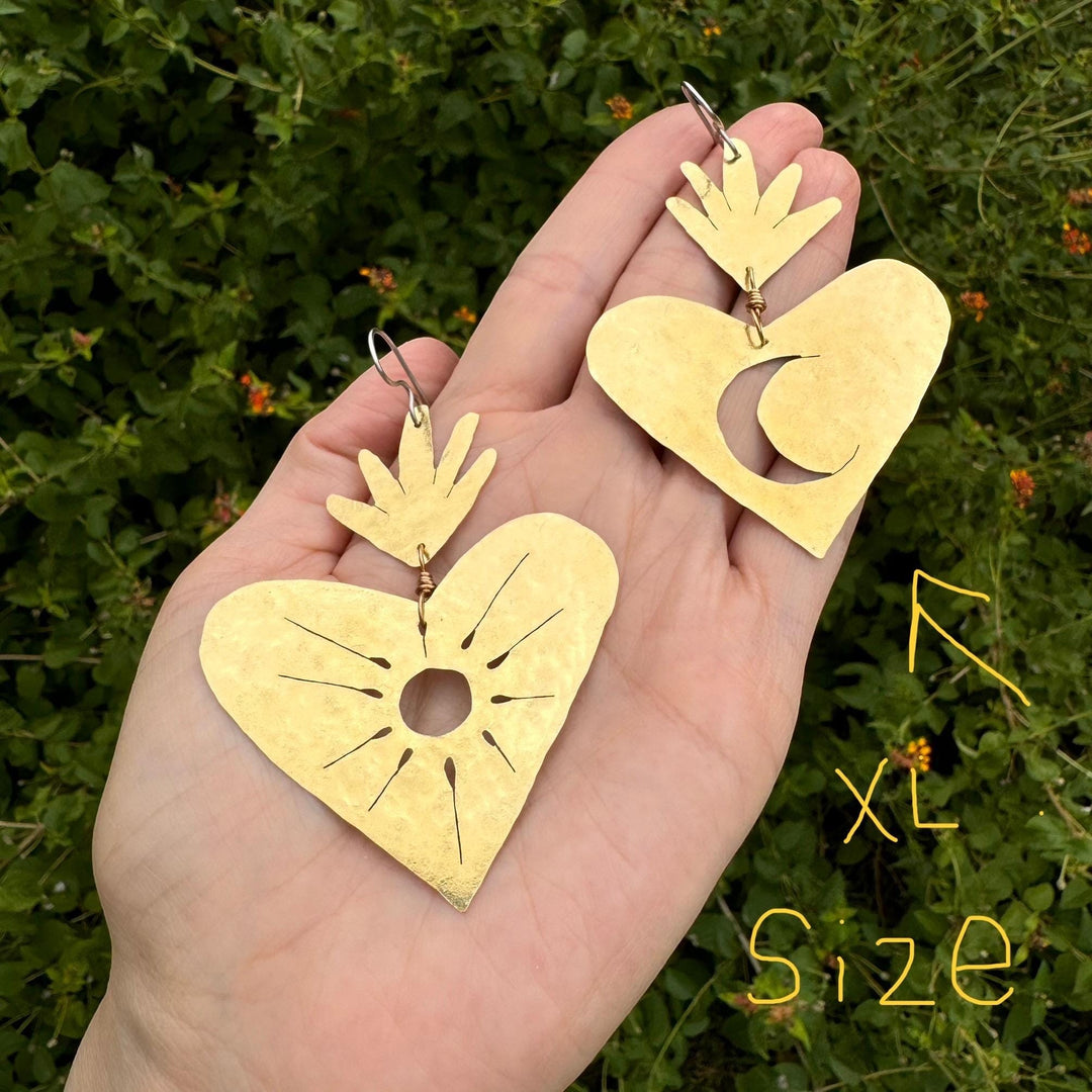 Sea Dragon Dreams XL sacred heart earrings with sun and moon cutouts, hand-hammered brass held in a palm