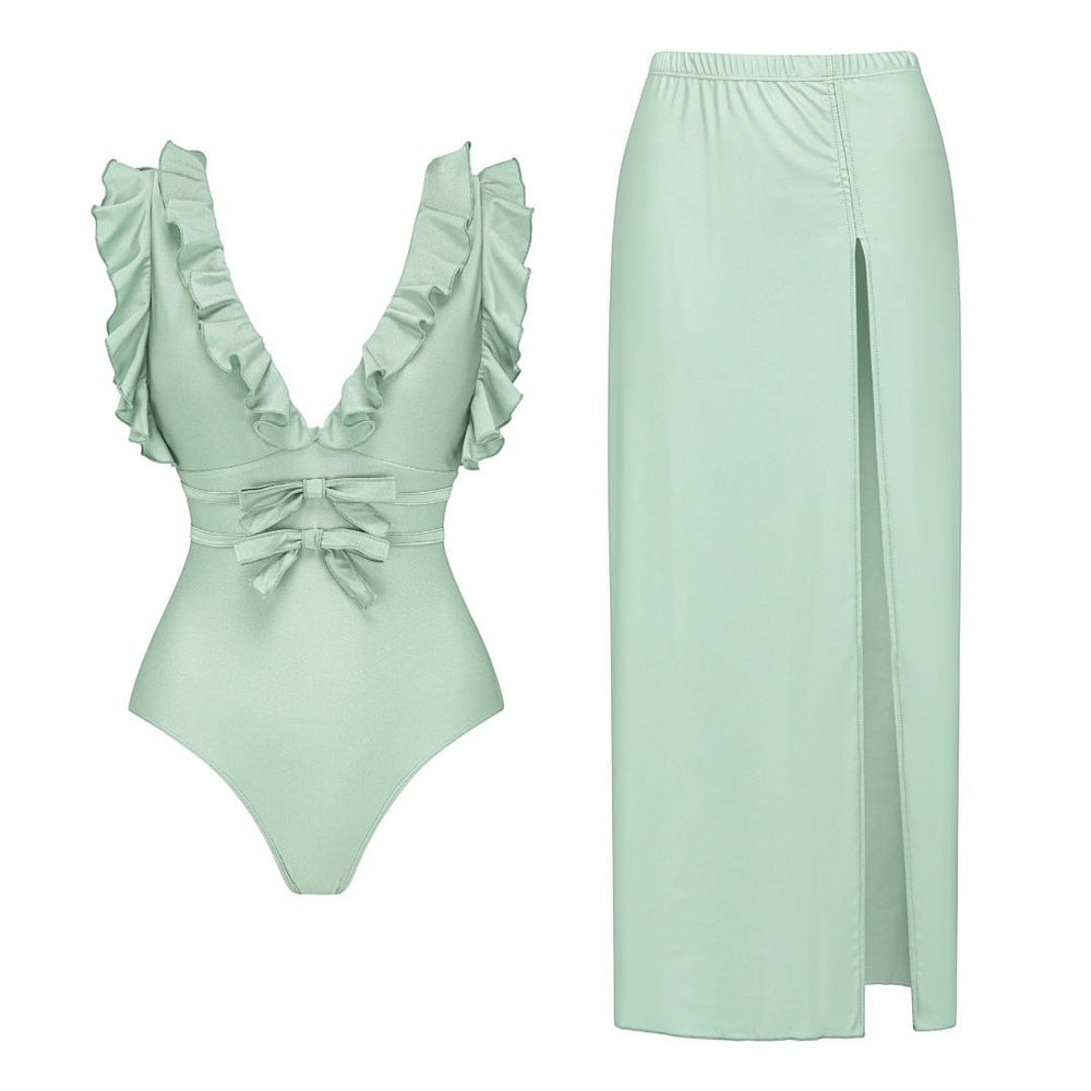 Sea Dragon Dreams sage green one-piece swimsuit with ruffled straps, bow accents, and a matching high-slit maxi skirt.