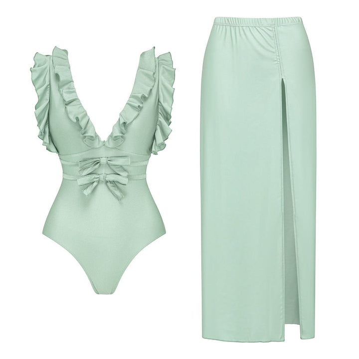 Sea Dragon Dreams sage green one-piece swimsuit with ruffled straps, bow accents, and a matching high-slit maxi skirt.