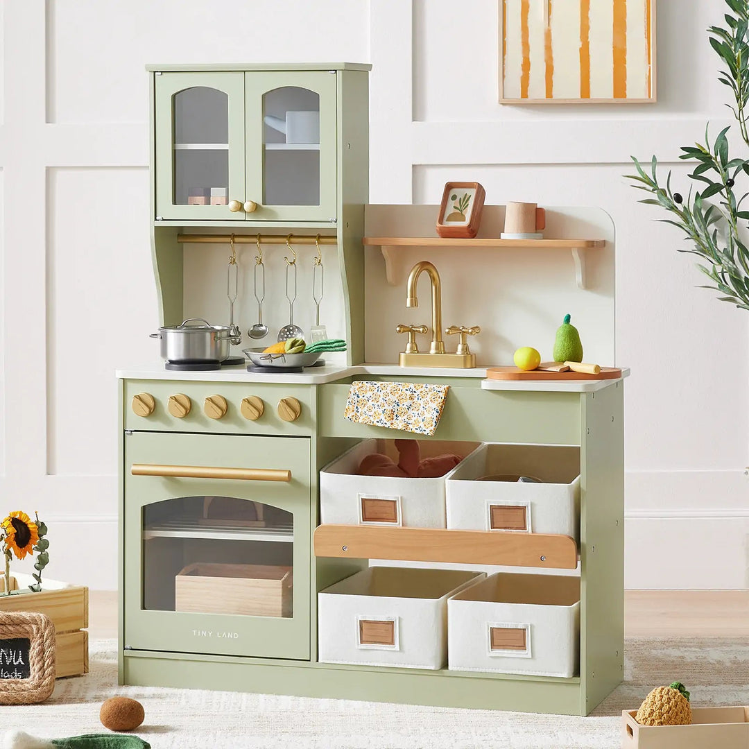 Sea Dragon Dreams Tiny Land wooden play kitchen in sage green with storage bins, toy cookware, and imitation faucet.