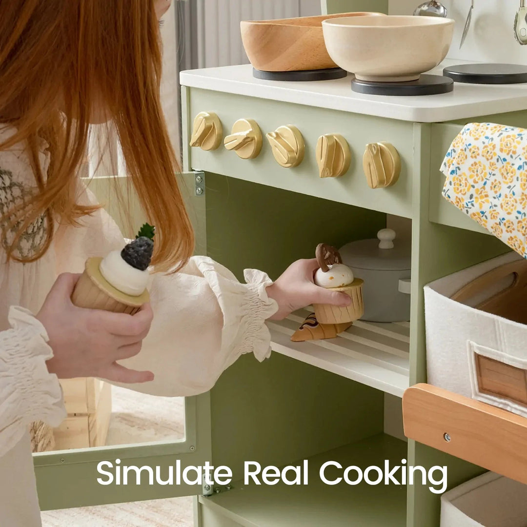 Sea Dragon Dreams Tiny Land wooden play kitchen in sage green with a child playing with toy cupcakes and cookware.