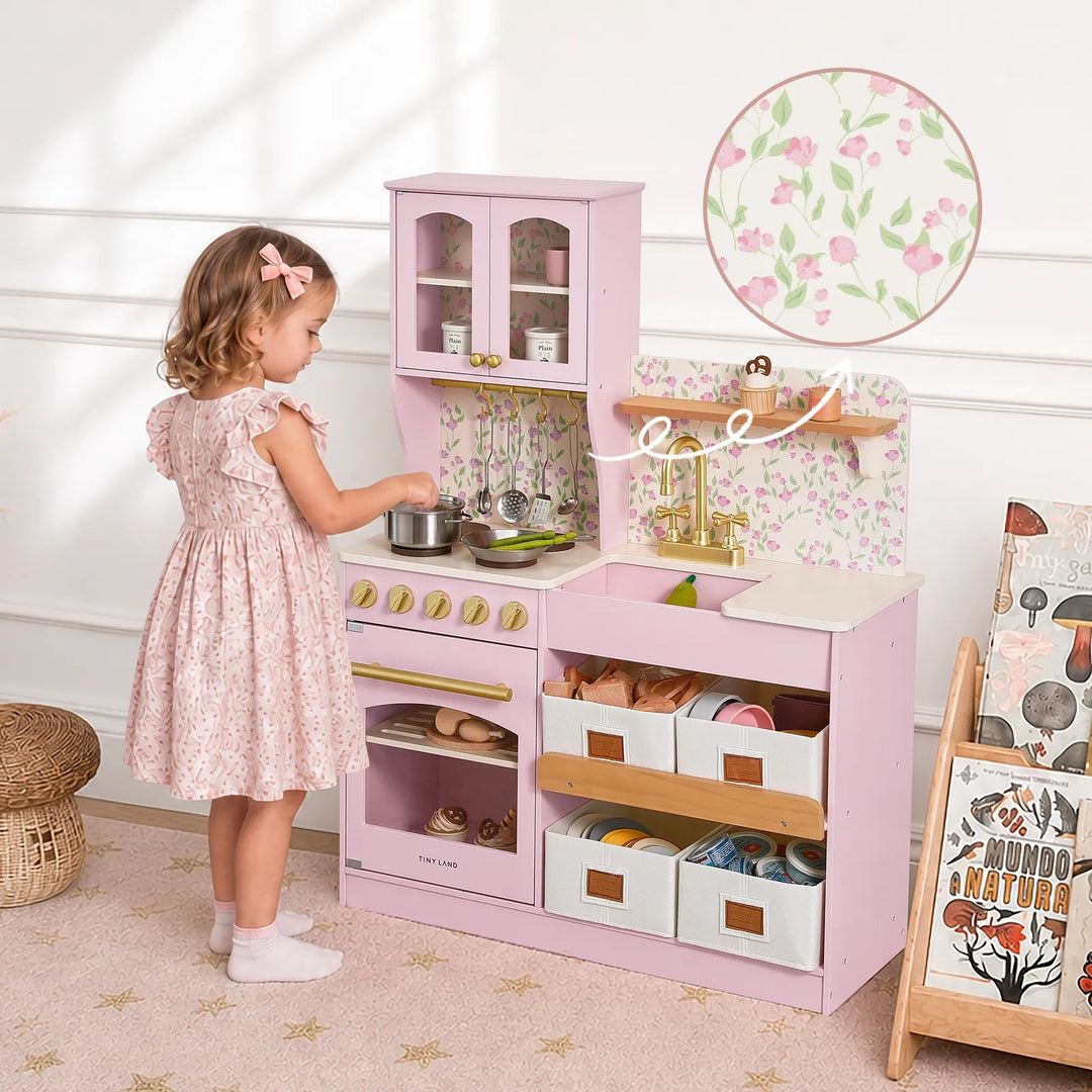 Sea Dragon Dreams Tiny Land wooden play kitchen in Sakura Pink with floral backsplash, gold hardware, and storage bins.
