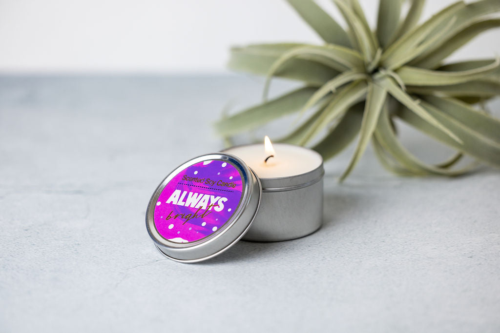 Sea Dragon Dreams scented soy candle in a silver tin with a purple Always Bright label, next to an air plant.