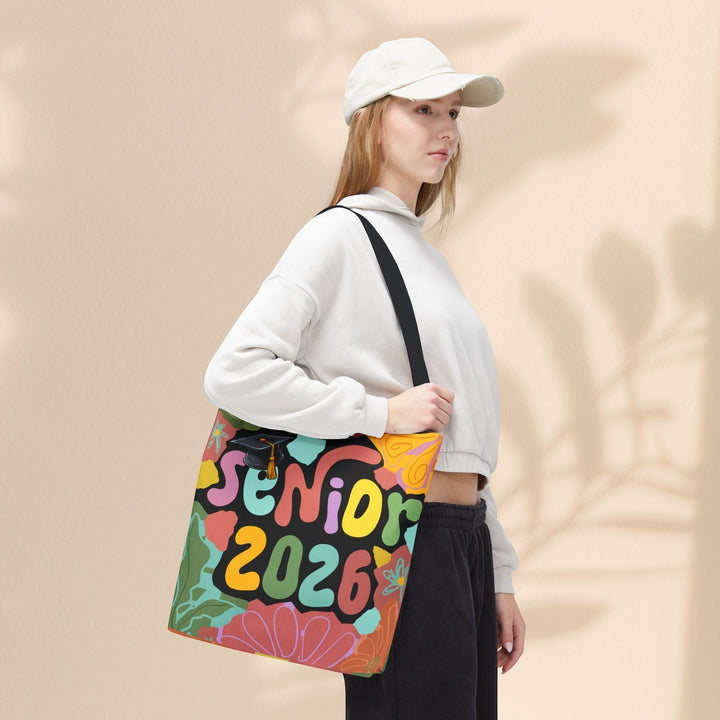 Sea Dragon Dreams Senior 2026 tote bag with colorful floral design and graduation cap, worn by a woman in a hoodie.