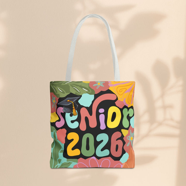 Sea Dragon Dreams Senior 2026 tote bag with colorful floral print, graduation cap, and white handles on beige wall.