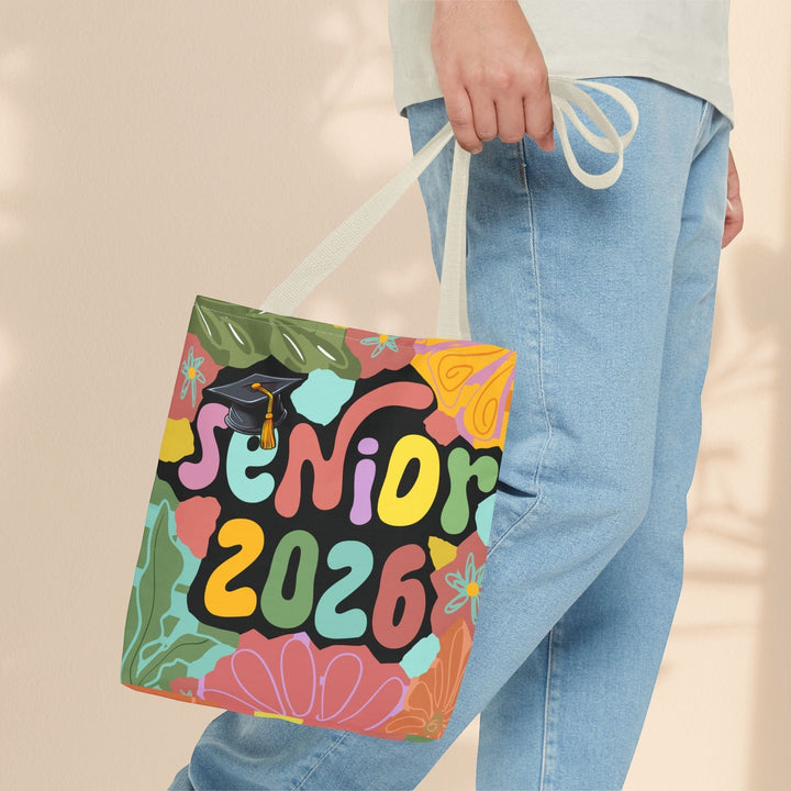 Sea Dragon Dreams Senior 2026 tote bag with colorful floral design and graduation cap held by a person in jeans.