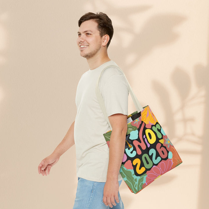 Sea Dragon Dreams Senior 2026 tote bag with colorful floral design carried over the shoulder by a smiling young man.