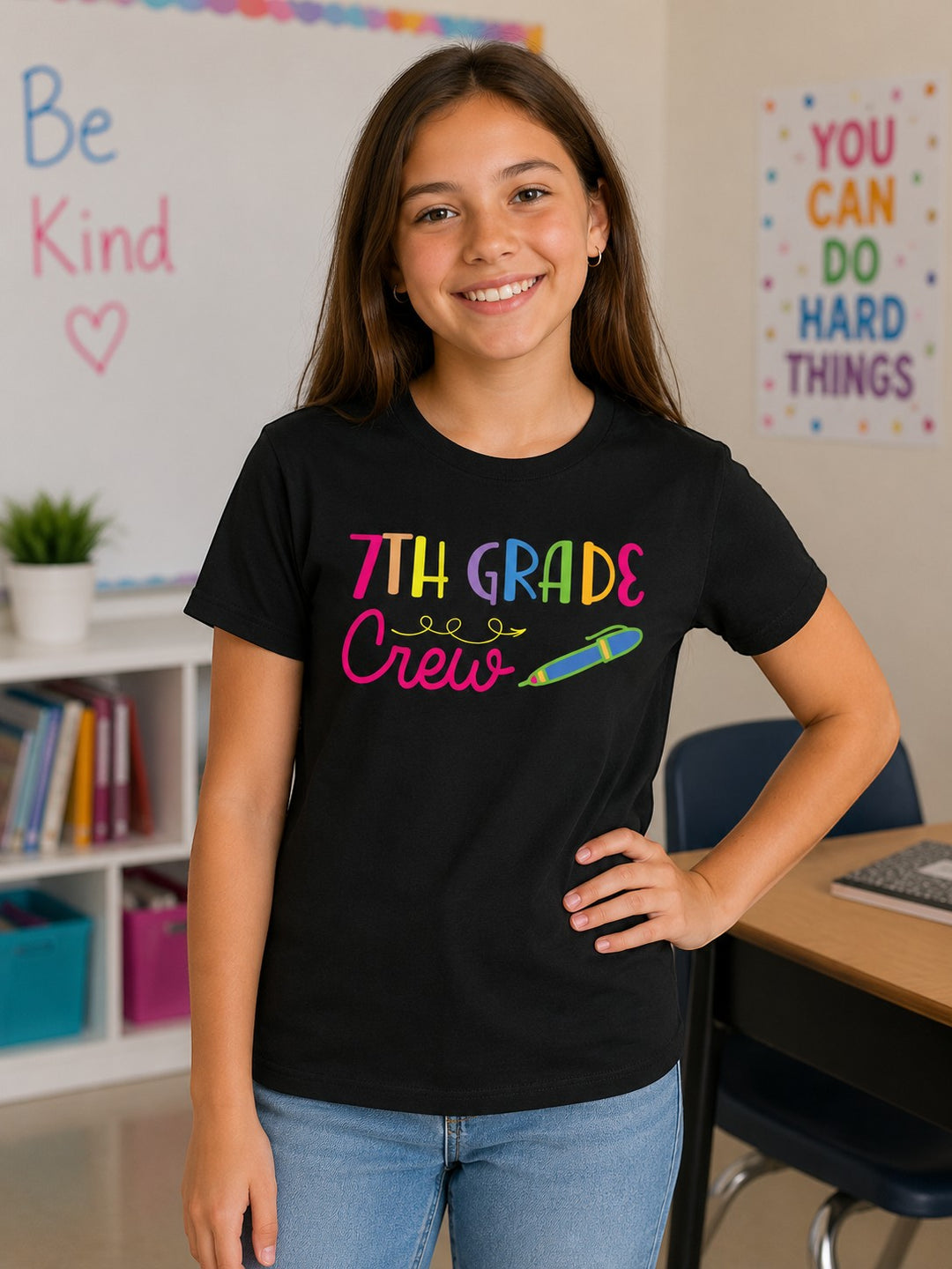 Sea Dragon Dreams black cotton t-shirt with colorful 7th Grade Crew graphic worn by a smiling student in a classroom.