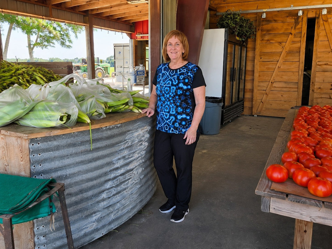 Woman wearing a Sea Dragon Dreams Shifting Blues sports jersey with a blue geometric pattern at a farm market.